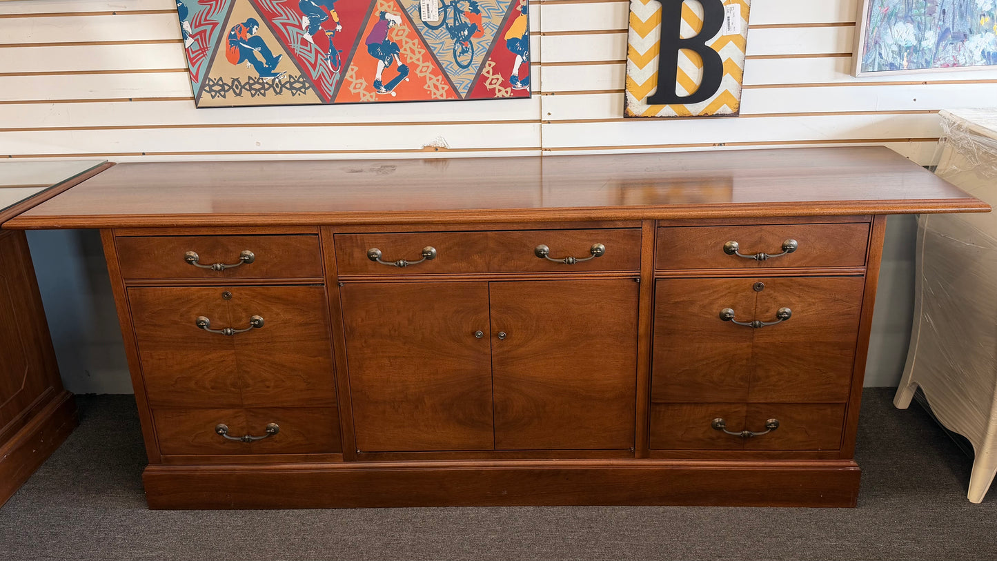 Wooden desk with multiple drawers and a glass top in a room setting.