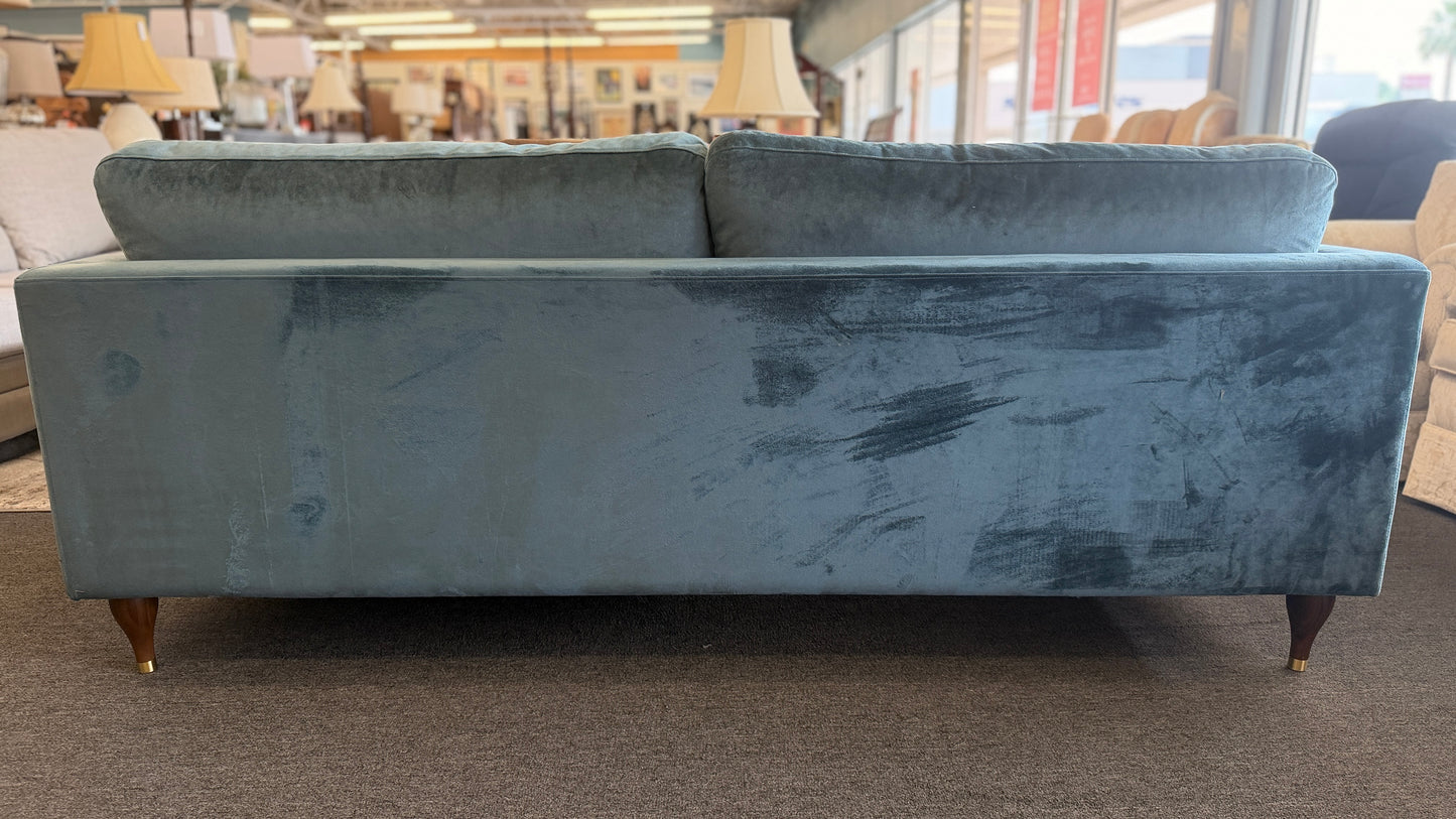 Blue velvet sofa in a store setting with other furniture visible.