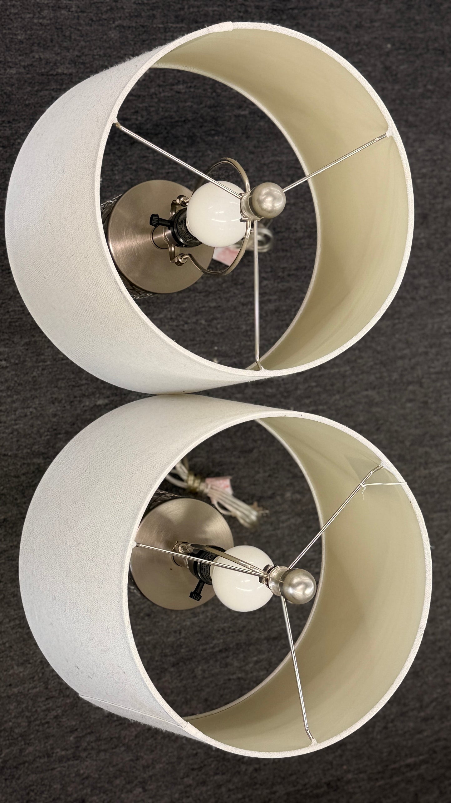 Two white lampshades with metallic fixtures on a dark background
