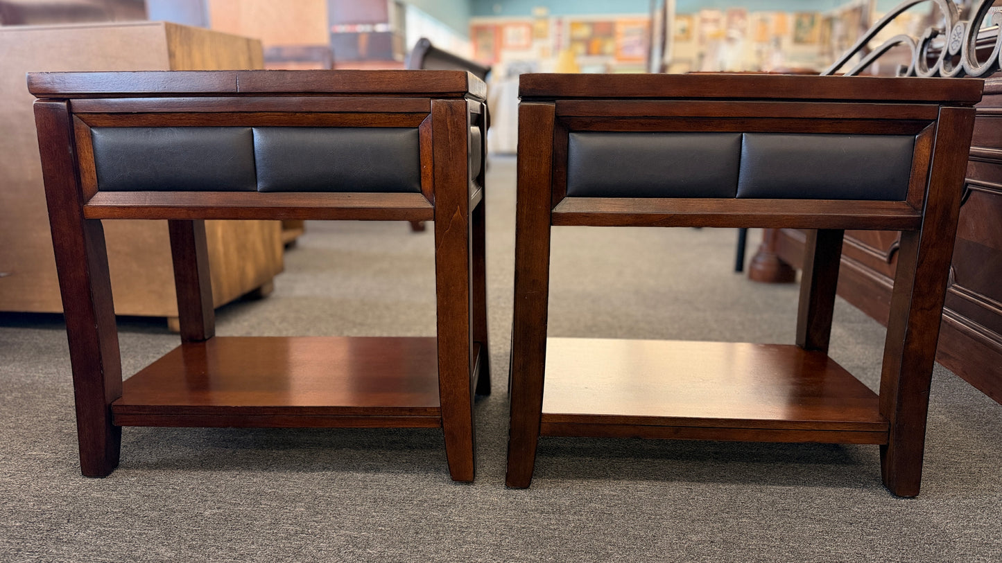 Two wooden side tables with leather seats in a showroom setting.