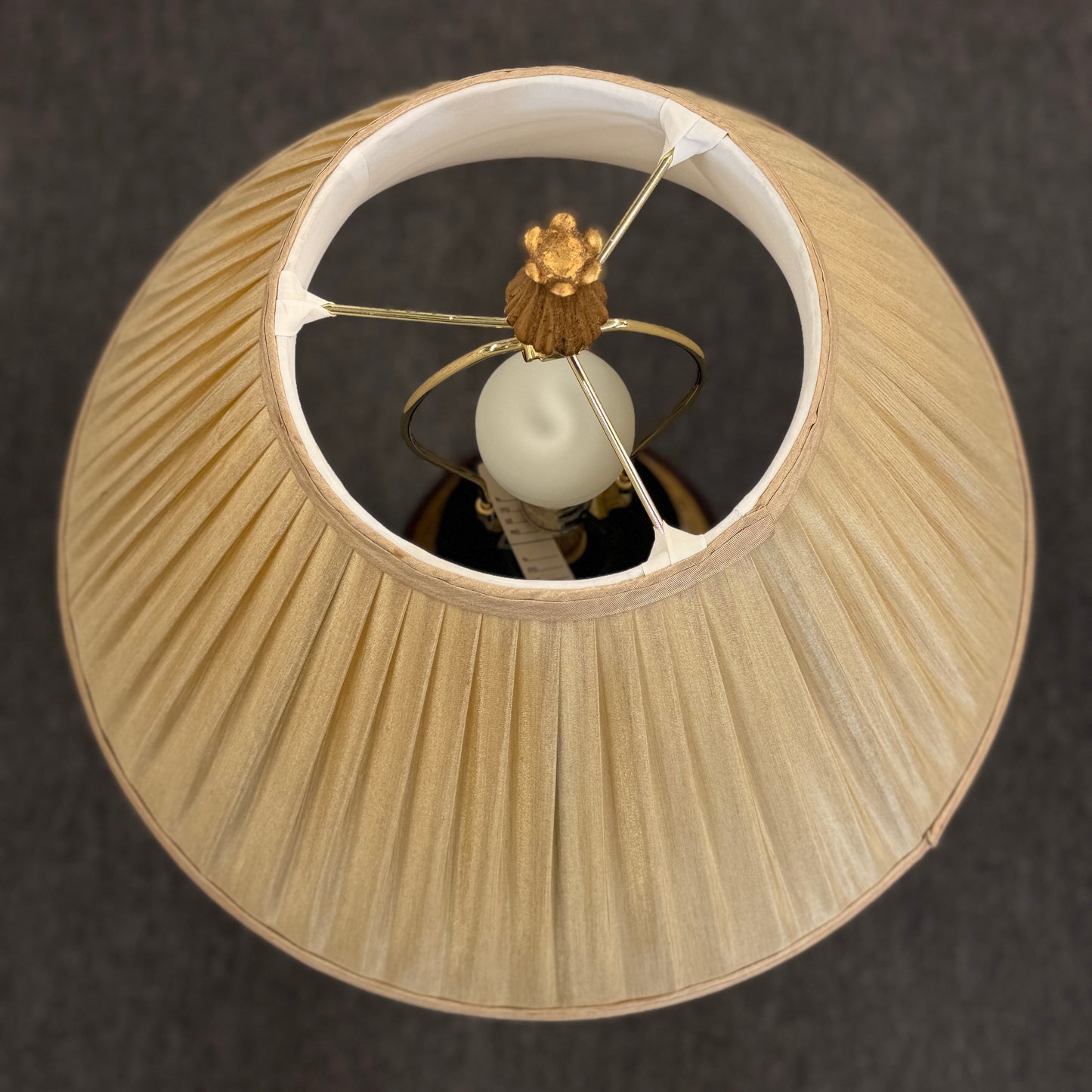 A traditional-style table lamp featuring an urn-shaped ceramic base with decorative gold-toned bands at the neck and base, topped with a pleated flared fabric lampshade.