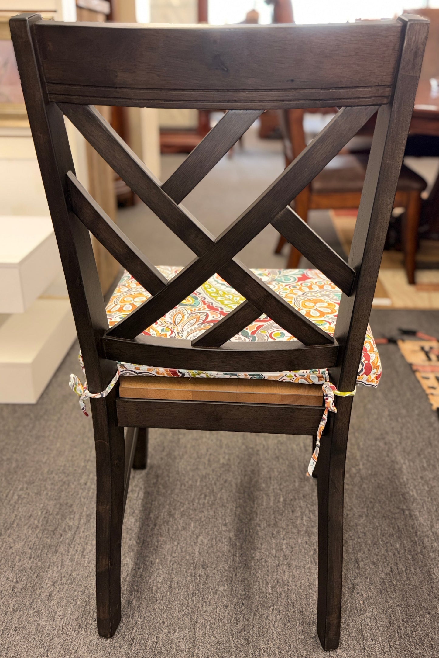 A casual oval dining table set featuring a mid-tone wood top, a dark base with an extendable leaf, and four matching X-back chairs with vibrant paisley-patterned tie-on cushions.