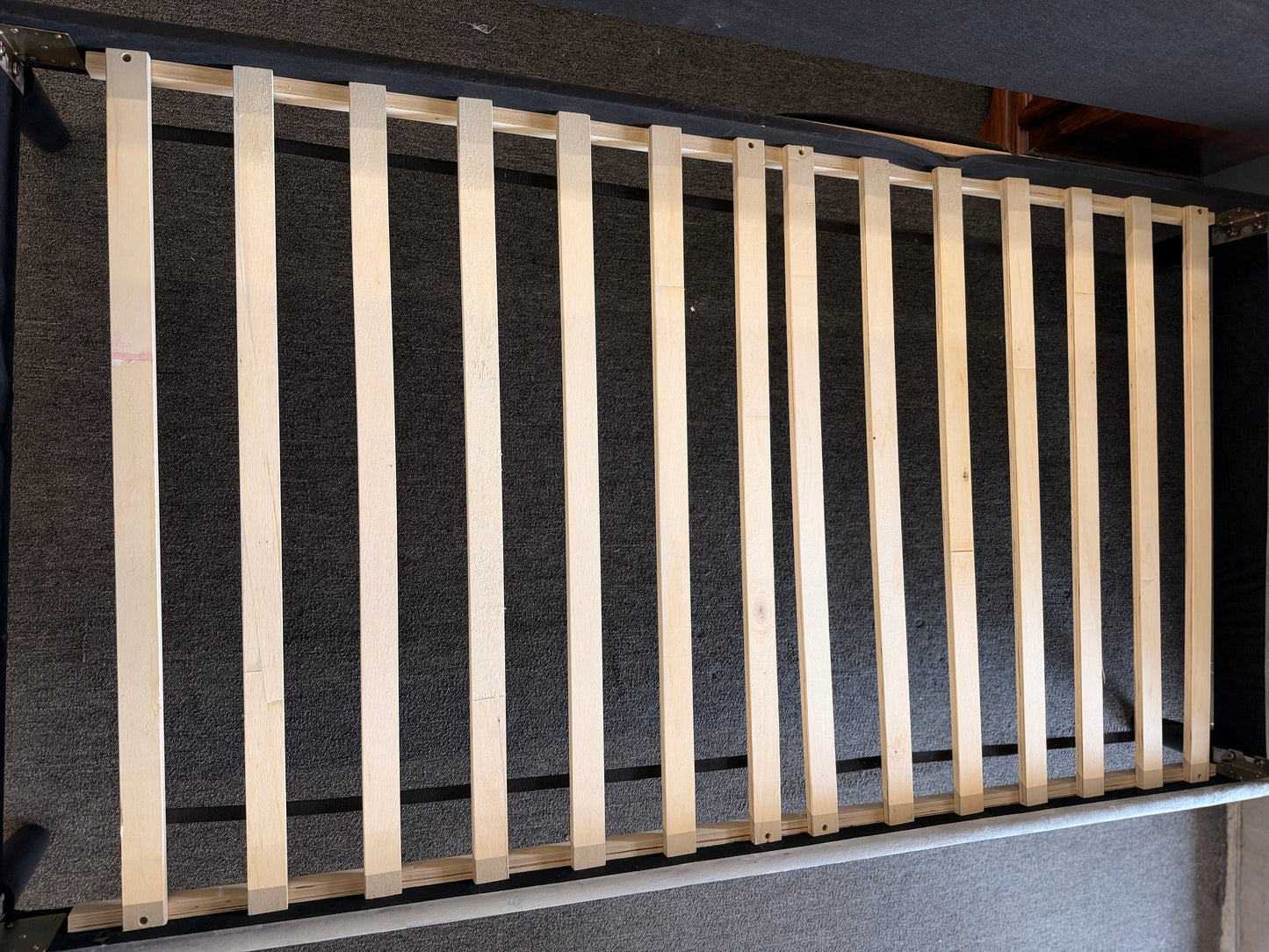 A modern daybed frame upholstered in a gray textured fabric, featuring a mid-height backrest, enclosed side panels, and a wooden slatted mattress support base.