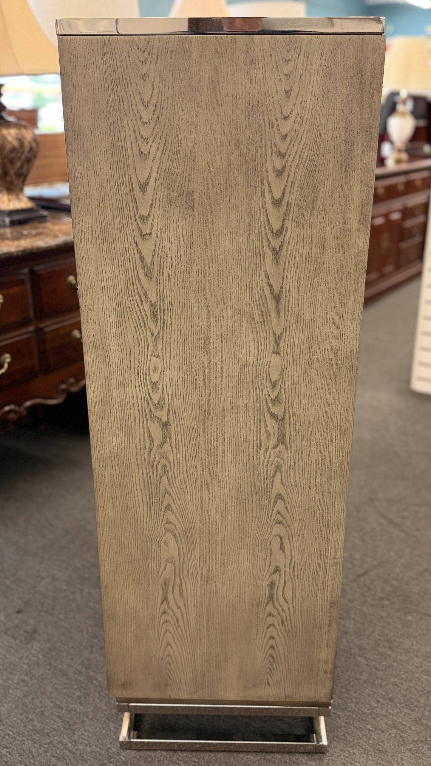 A contemporary tall 7-drawer highboy chest of drawers with a soft gray-washed wood grain finish, minimalist silver hardware, and a geometric chrome base.