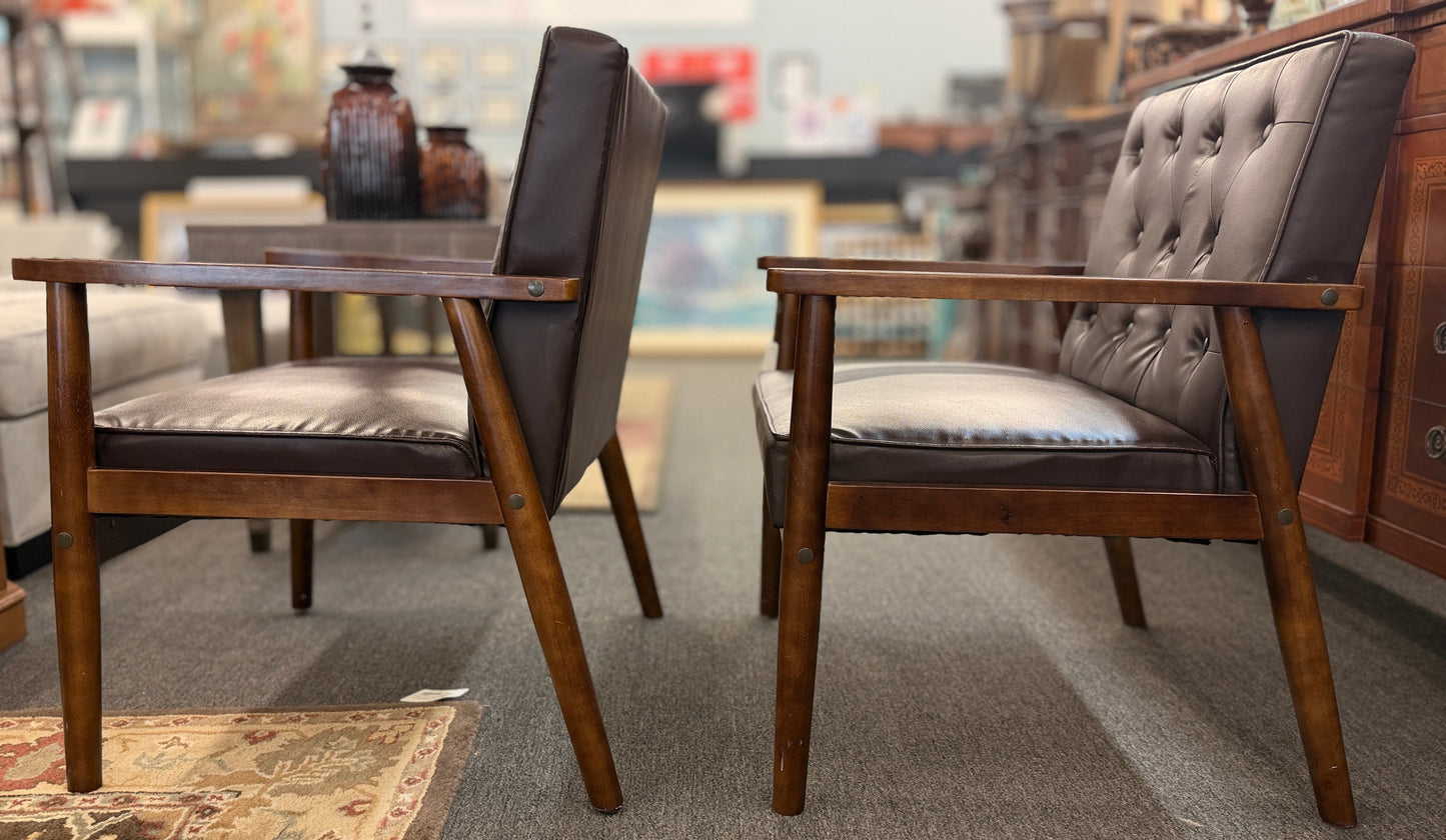 A pair of mid-century modern style accent armchairs featuring dark brown button-tufted backrests, smooth seat cushions, and exposed medium-toned wooden frames with tapered legs.
