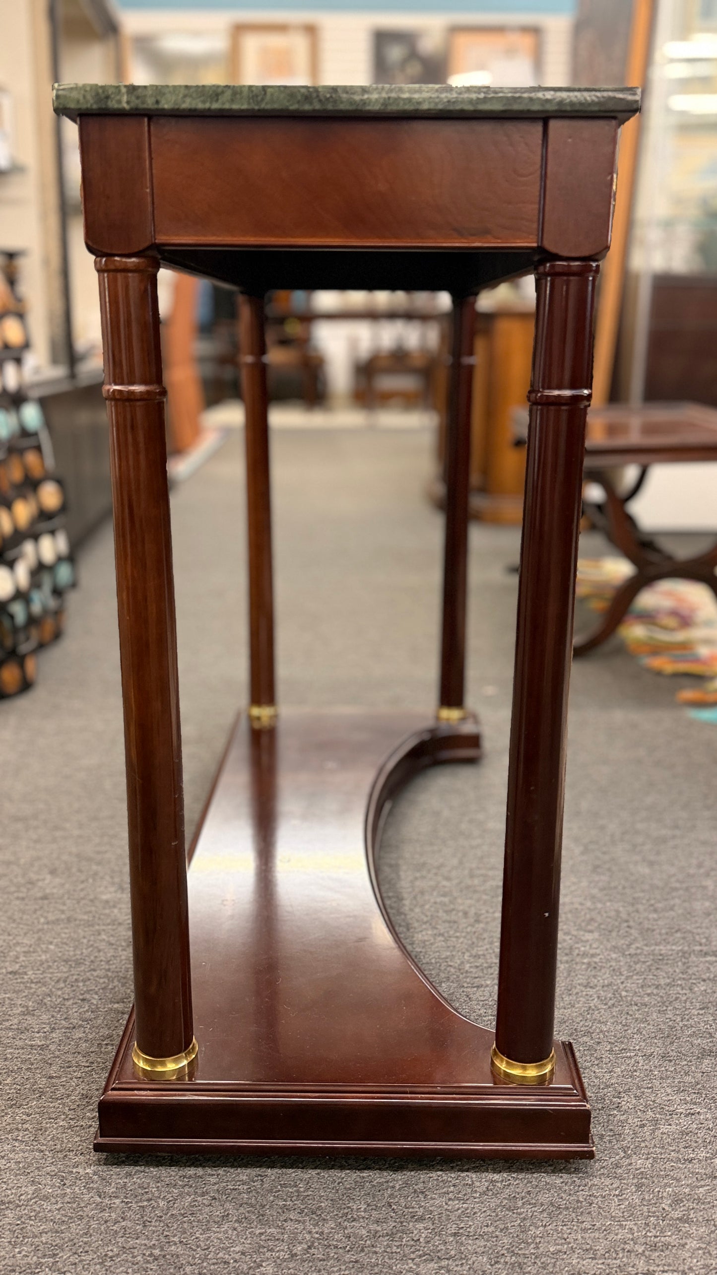 Traditional console table with a rectangular green marble top, dark wood frame, fluted cylindrical legs, gold-toned brass rosette accents, and a solid wood base plinth.