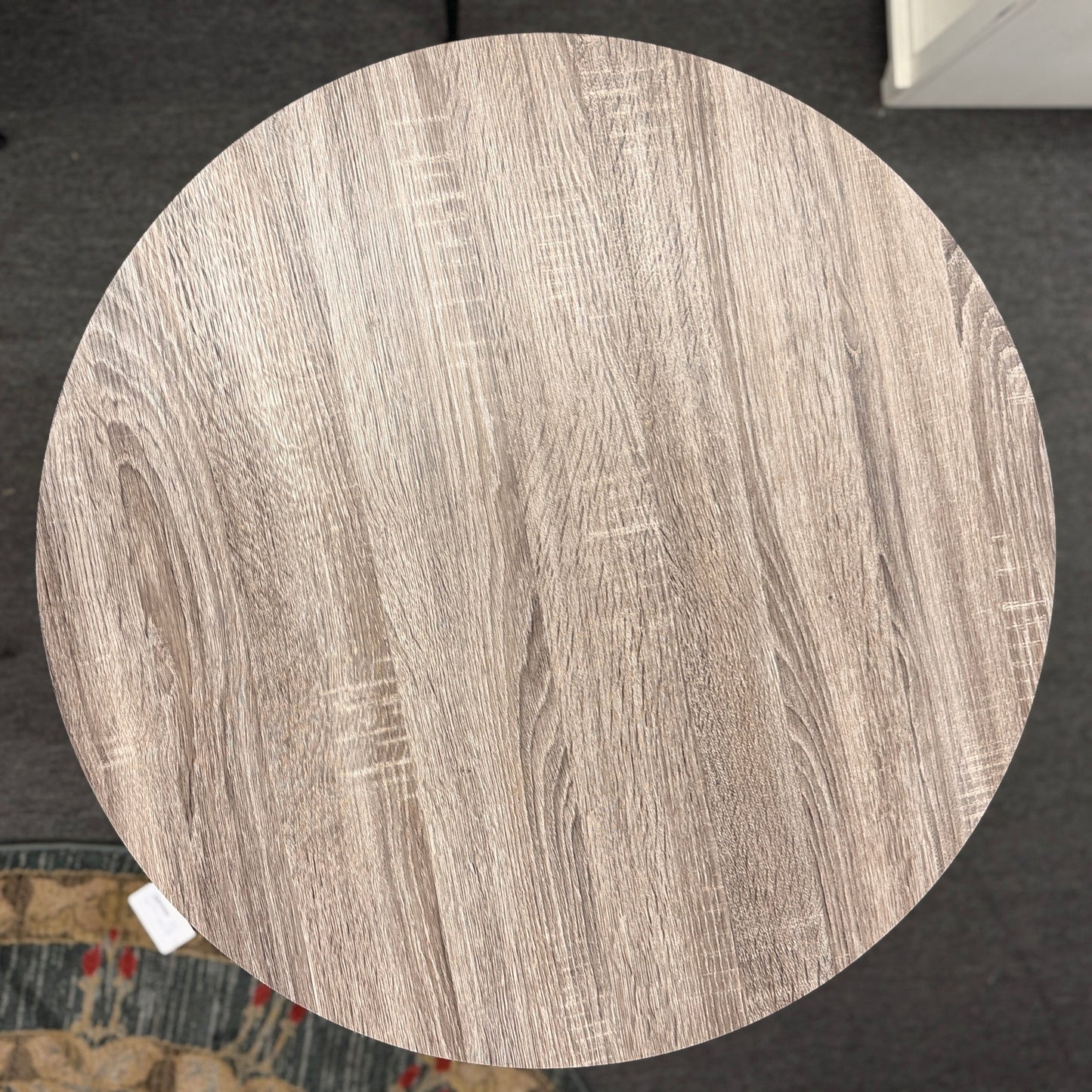 Round pub table with a light brownish-grey faux wood grain top and a dark metal pedestal base featuring curved intersecting legs.