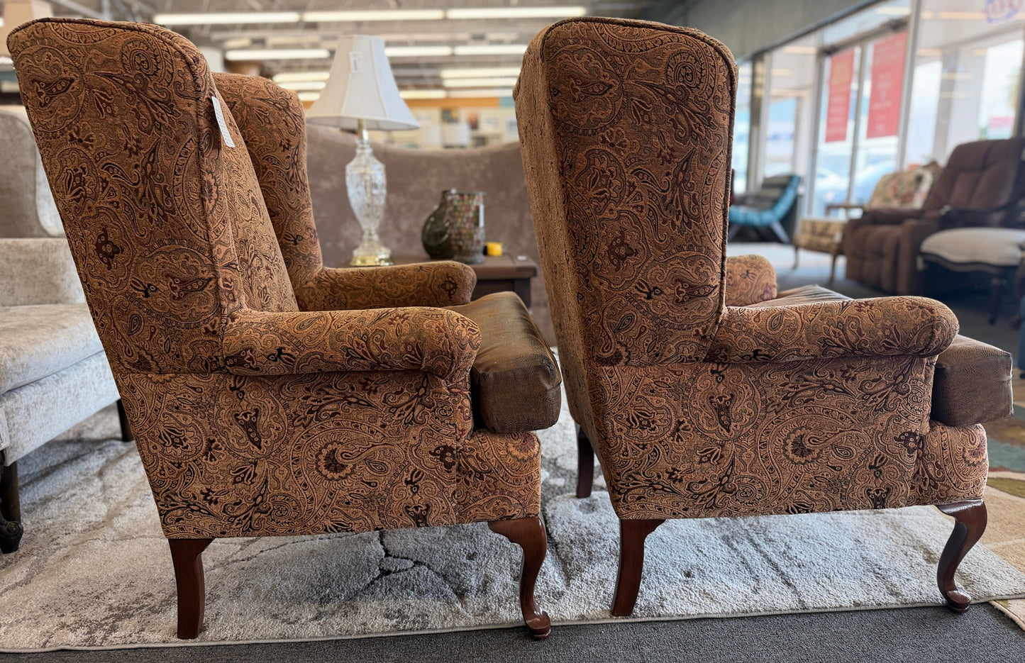 Pair of traditional wingback accent chairs upholstered in tan and brown paisley fabric with curved Queen Anne-style wooden legs.