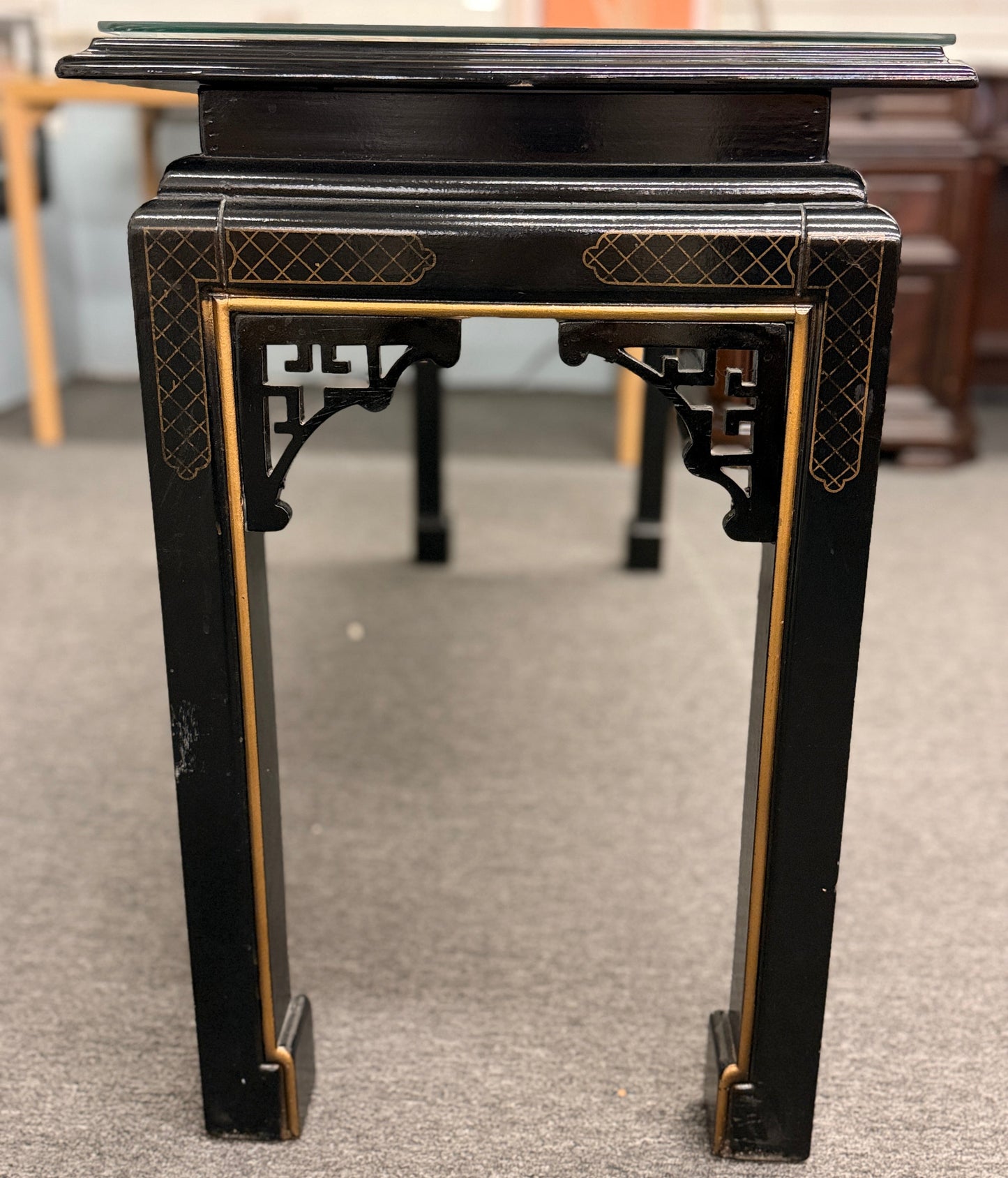 Black lacquer console table featuring hand-painted Asian-inspired scenes with figures, architecture, and landscapes beneath a protective clear glass surface.