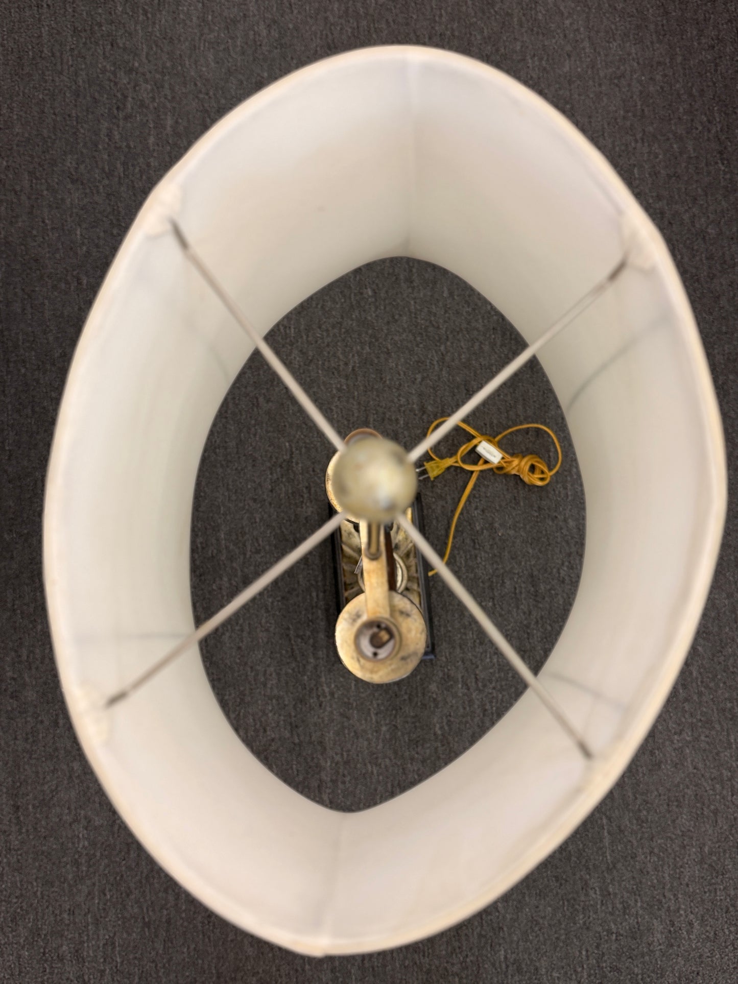 Decorative table lamp featuring a dark U-shaped body with metallic leaf accents, a fluted metallic pedestal, black square base, and a large cream-colored drum shade.
