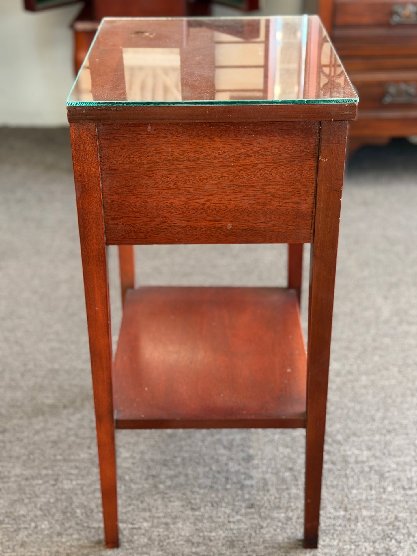 A Federal-style wood accent table featuring fluted corner accents, an arched apron, an oval rosette drop pull, an open lower shelf, and a glass top in good condition.