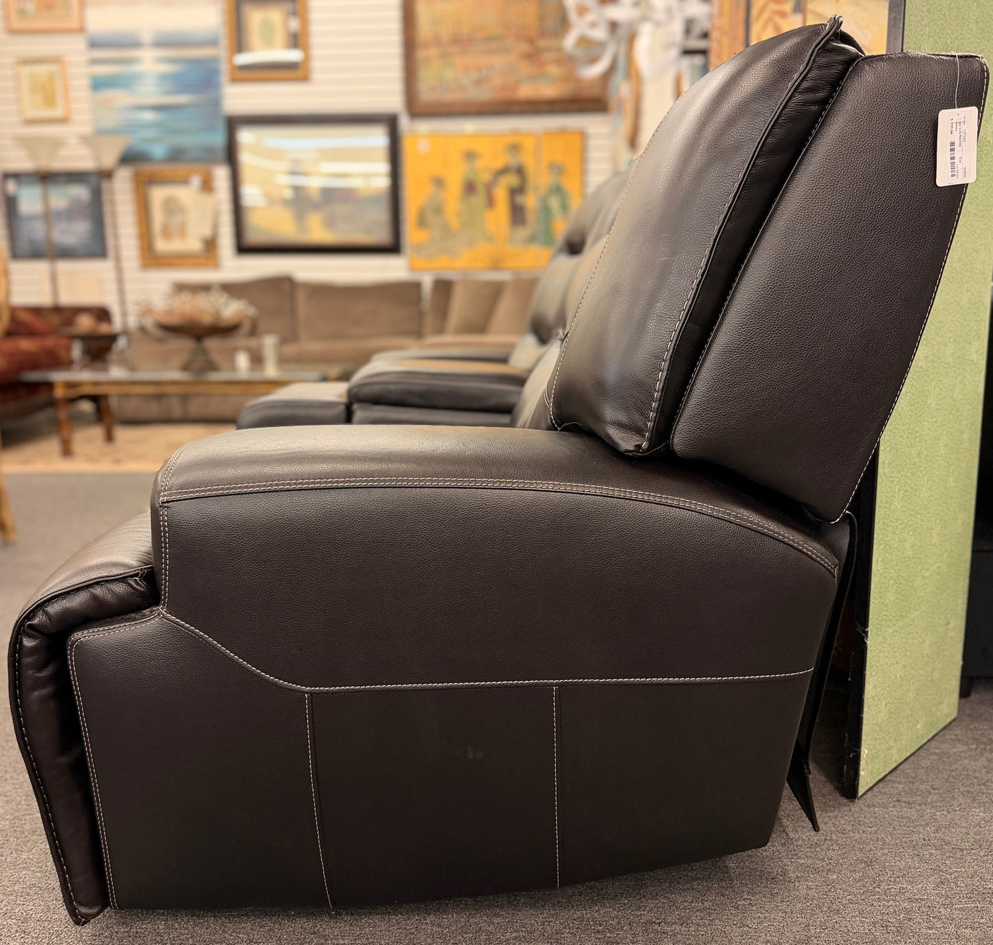 Brown dual power reclining loveseat upholstered in leather with prominent stitched detailing, independent reclining seats, and a center storage console with padded armrests.