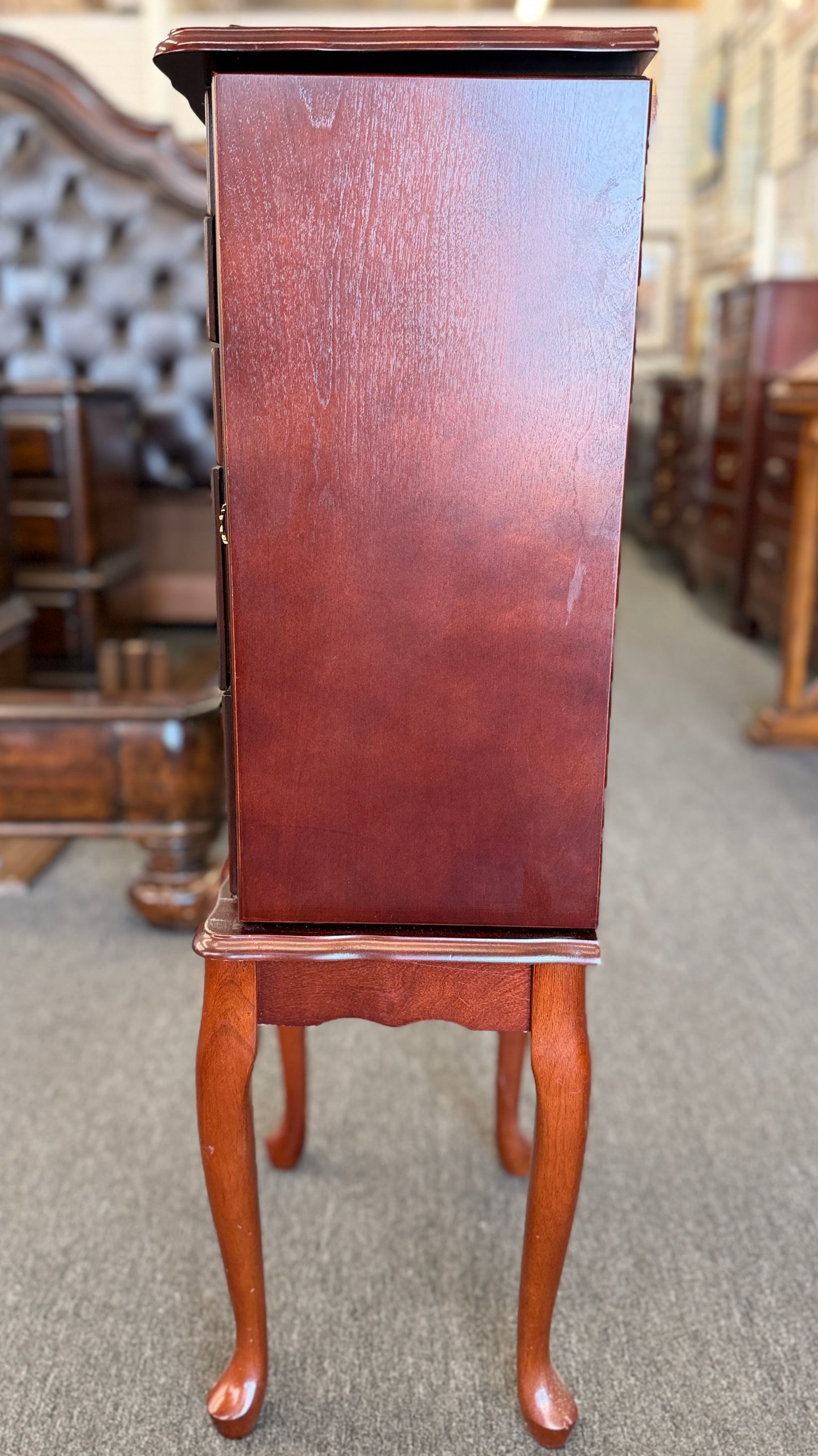 A tall cherry-finished wooden jewelry cabinet on cabriole legs featuring pull-out drawers, swinging side doors, and a flip-top vanity mirror.