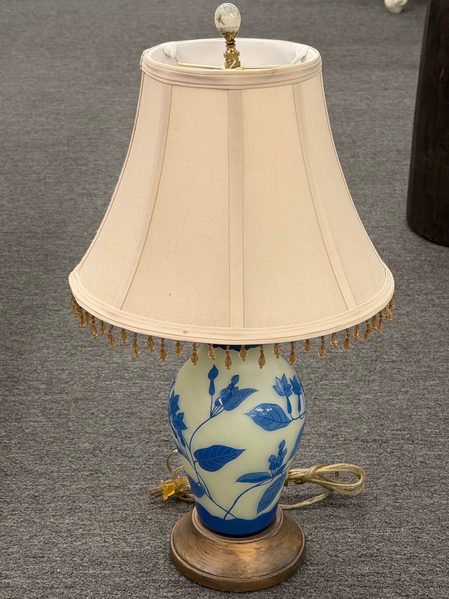 Traditional Chinoiserie blue and cream floral table lamp featuring a ceramic base with a blue floral design and a beige lampshade with beaded fringe decorative trim at 2nd Debut Houston consignment showroom