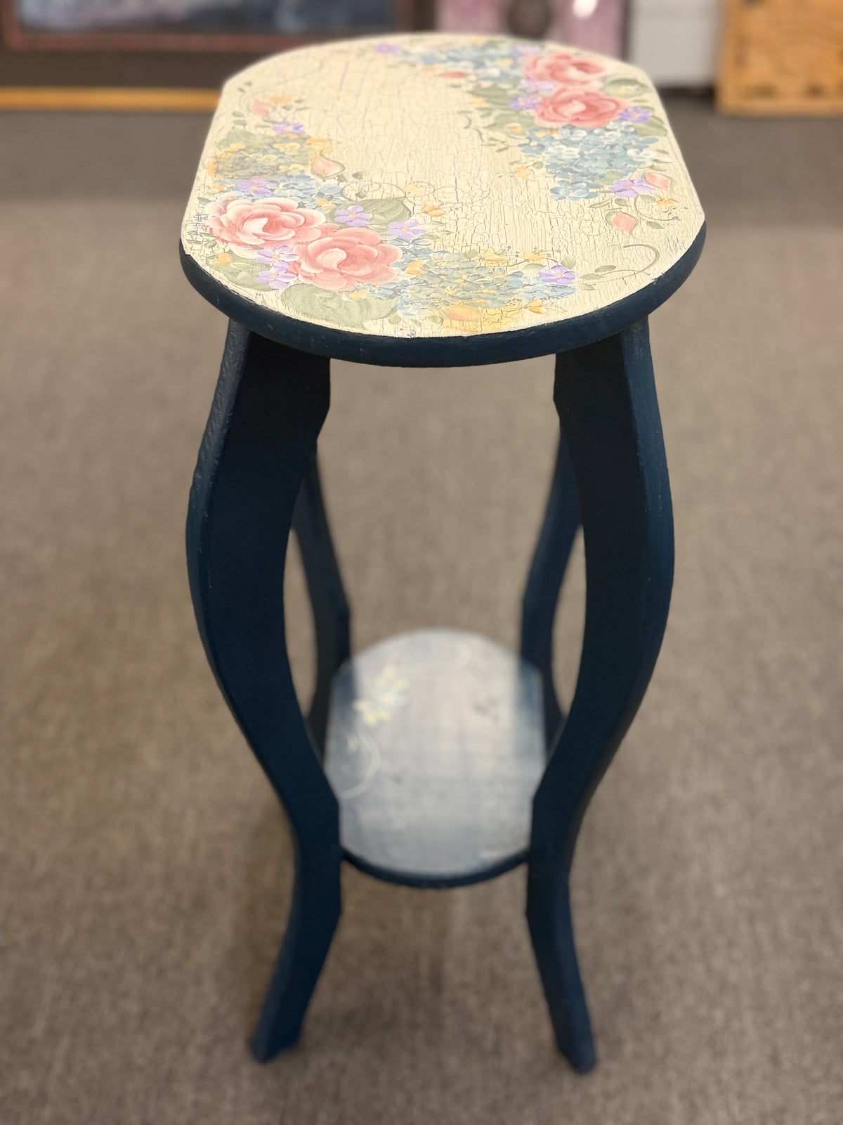 A dark blue accent table decorated with painted floral motifs on both the top surface and the lower shelf in good condition.