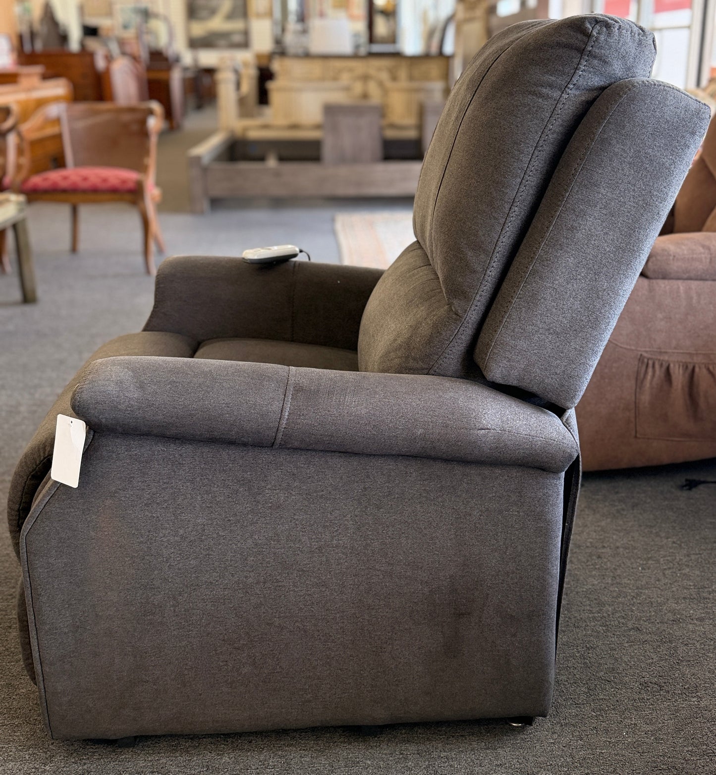 A standard upholstered recliner chair in a solid grayish-brown fabric featuring a structured paneled backrest and padded armrests.