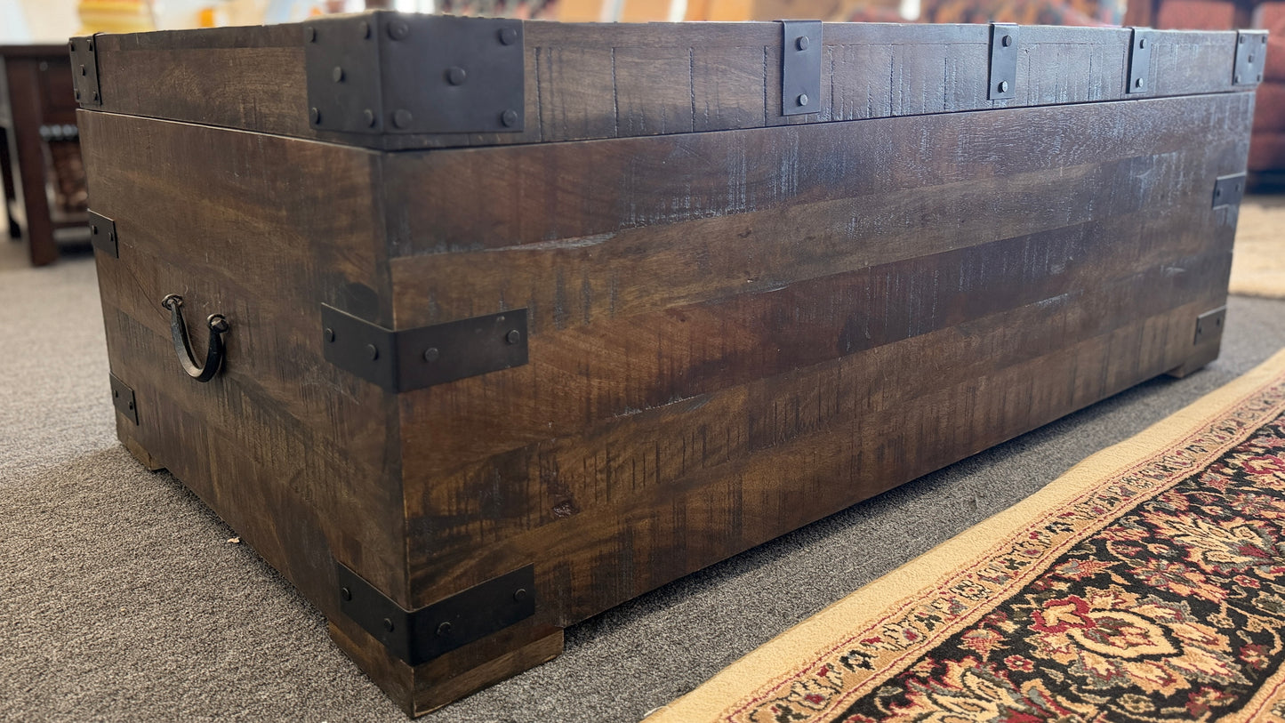 A rustic industrial trunk coffee table made of distressed dark wood with black iron corner brackets, open partially to reveal a lift-top mechanism and internal storage space.