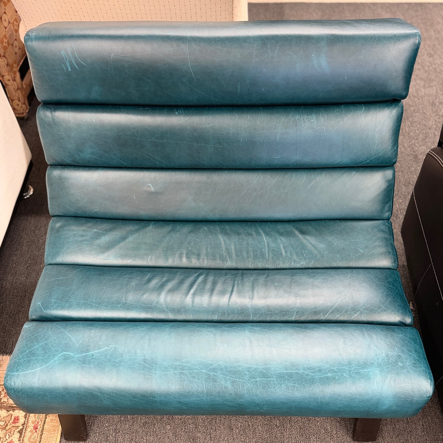 Modern armless accent chair upholstered in distressed teal leather featuring horizontal channel tufting and dark square wooden legs.