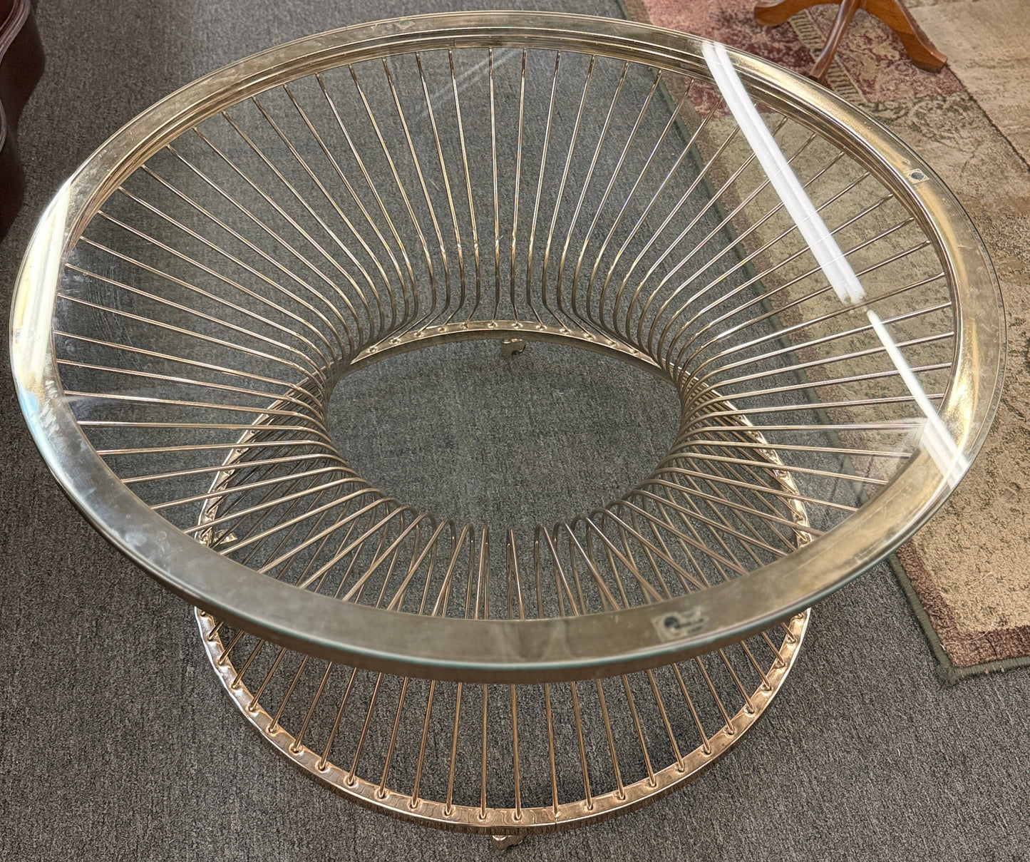 Modern round coffee table featuring a clear glass top and a sculptural flared wire-spoke metal base with a light, airy design.