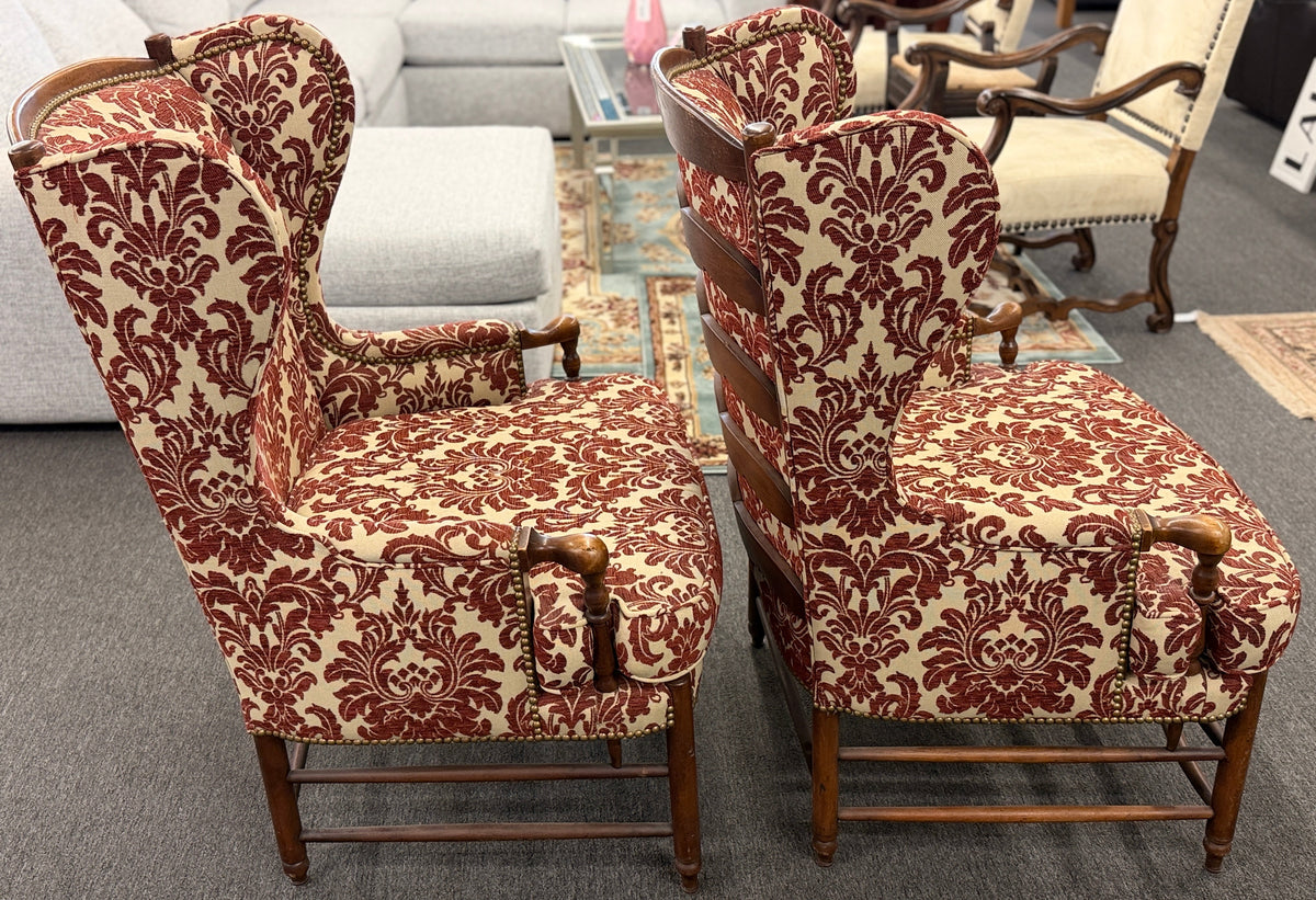 Pair of classic wingback armchairs upholstered in a bold burgundy and cream damask floral pattern detailed with nailhead trim and carved wooden legs in good condition.