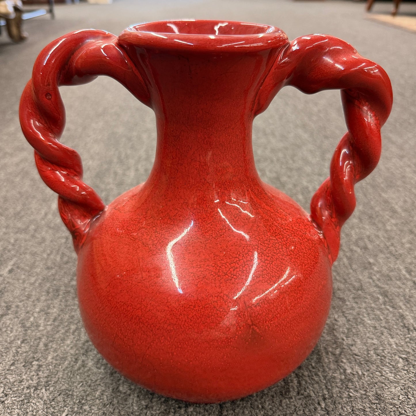 A red crackle-glazed ceramic urn vase featuring two twisted rope handles and a bulbous body in excellent condition.