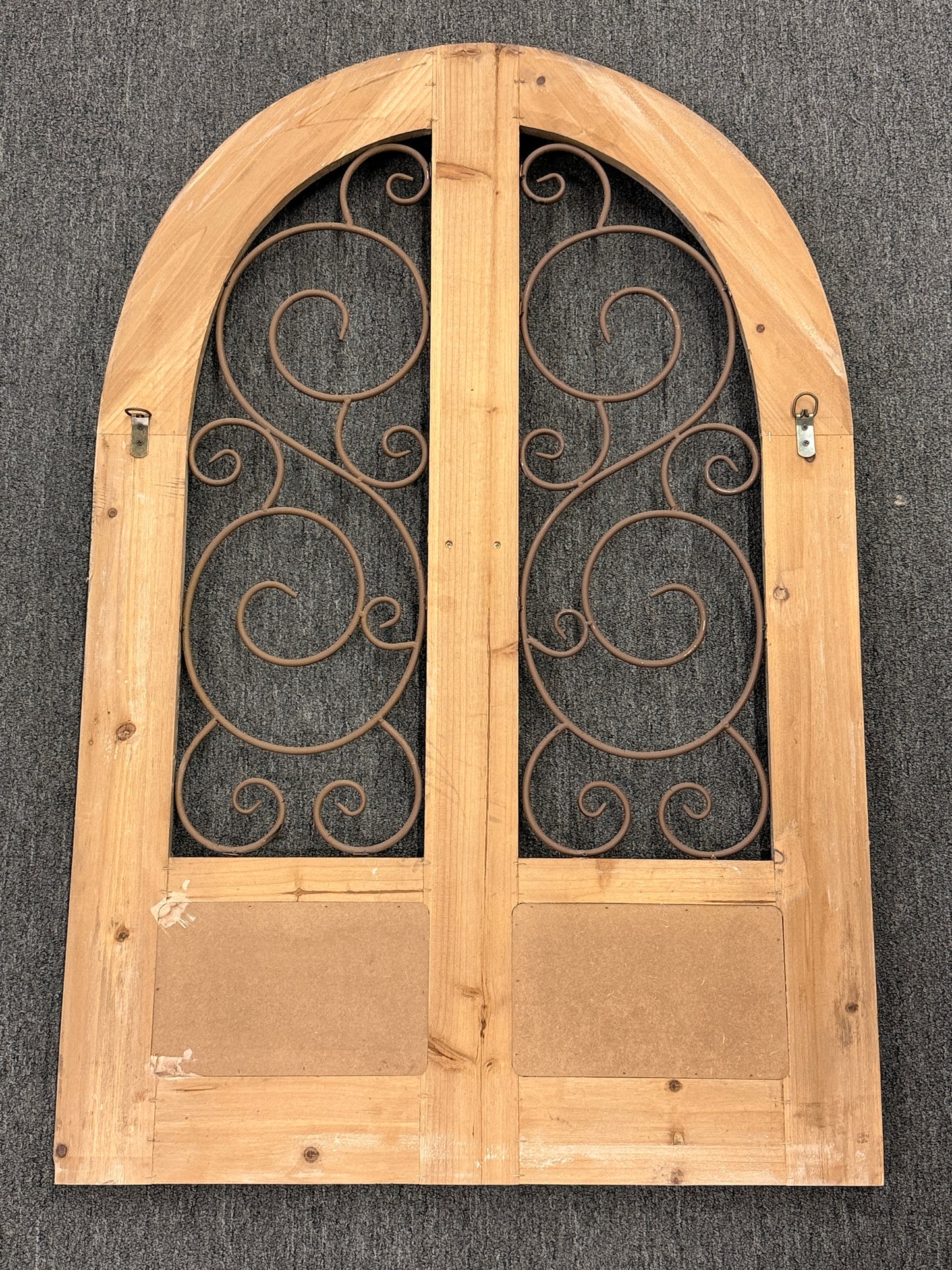 A large arched decorative wall panel designed like a rustic Tuscan door with a distressed wood frame and dark metal scrollwork gating.