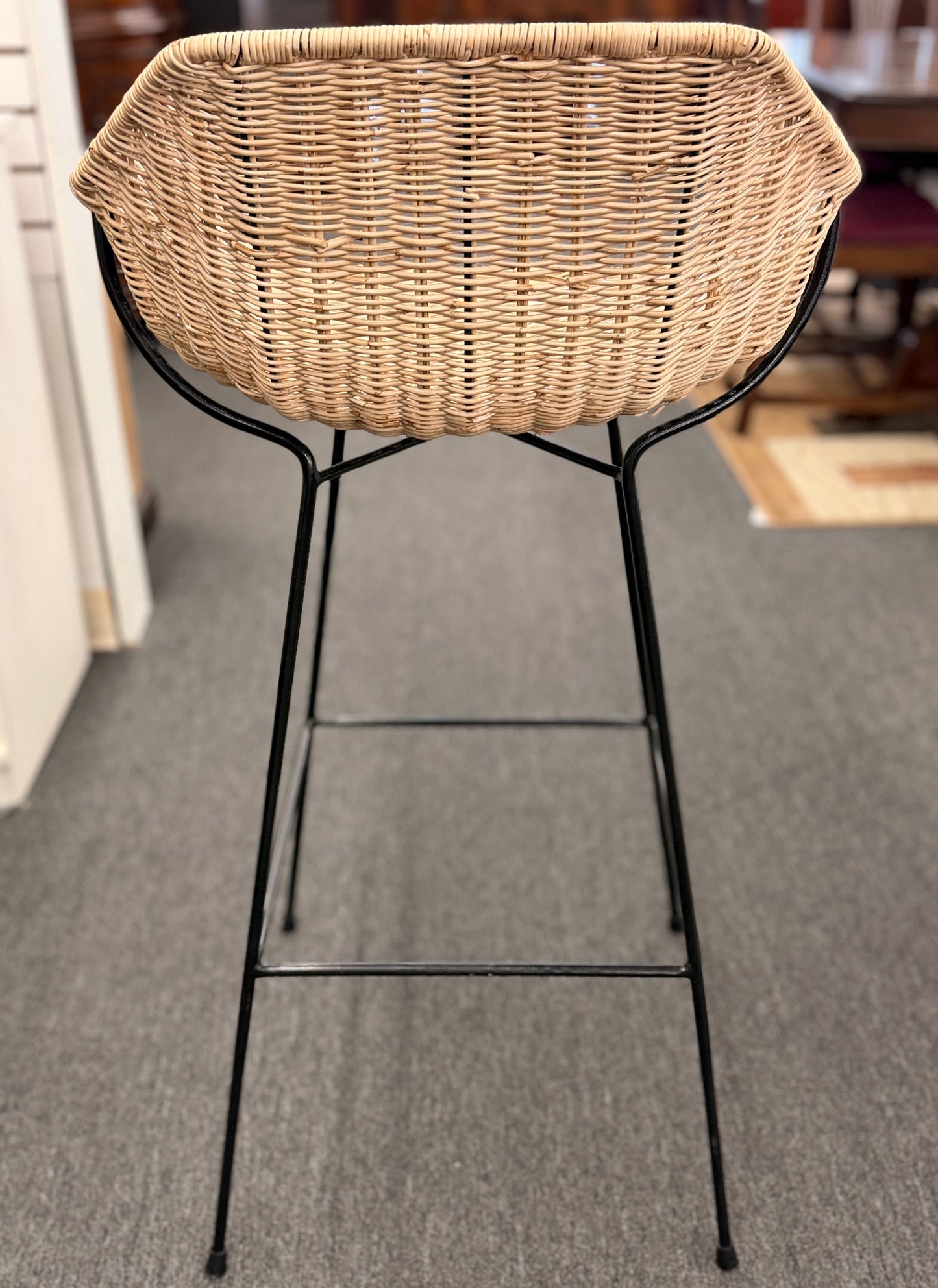 Set of three modern bar stools featuring woven rattan bucket-style seats, slim black iron frames, and built-in footrests.