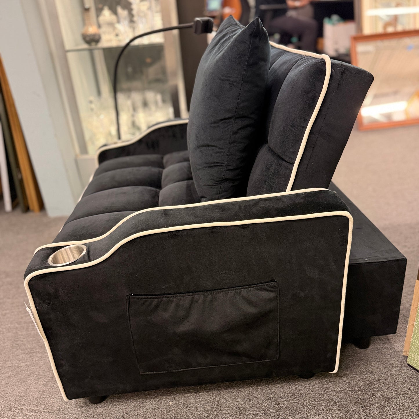 Plush theater-style sleeper chair upholstered in fabric with contrast piping, built-in cup holders, an adjustable reading light, and a matching throw pillow.