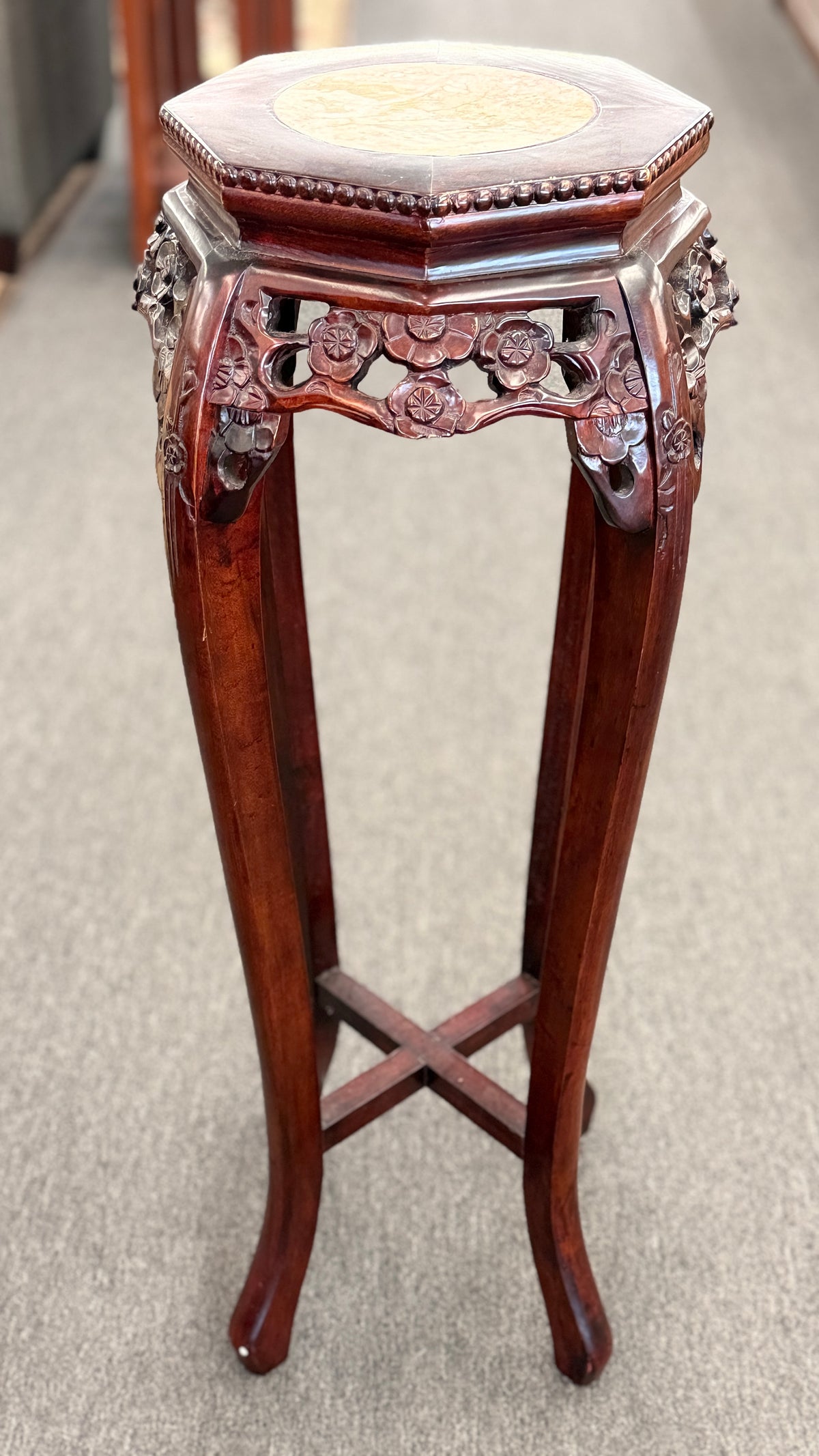 A traditional Asian-style tall dark wood plant stand featuring a hexagonal marble inset top, pierced floral apron, and curved legs with an X-stretcher base in good condition.