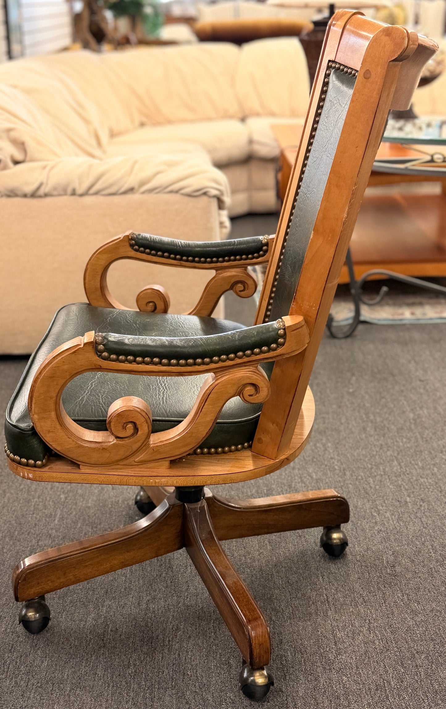 A traditional executive-style office desk chair with polished wood frame, deep forest green faux leather upholstery, brass nailhead trim, and a wheeled swivel base.