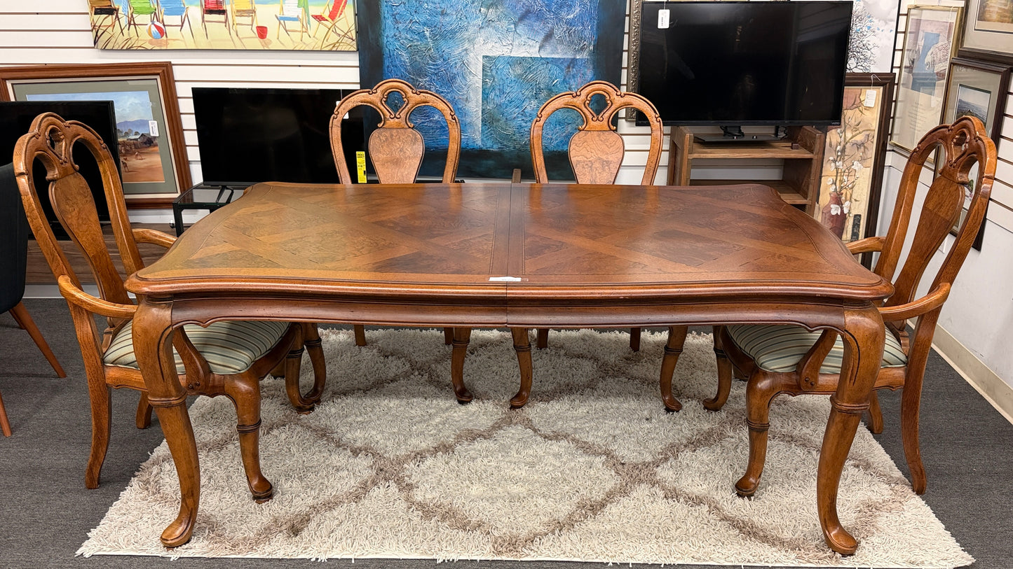 A 7-piece formal dining set featuring a marquetry wood inlay rectangular table with cabriole legs and six carved chairs with striped seats.