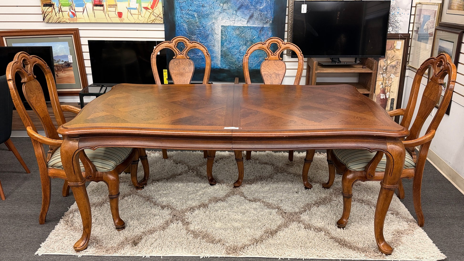 A 7-piece formal dining set featuring a marquetry wood inlay rectangular table with cabriole legs and six carved chairs with striped seats.