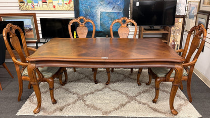 A 7-piece formal dining set featuring a marquetry wood inlay rectangular table with cabriole legs and six carved chairs with striped seats.
