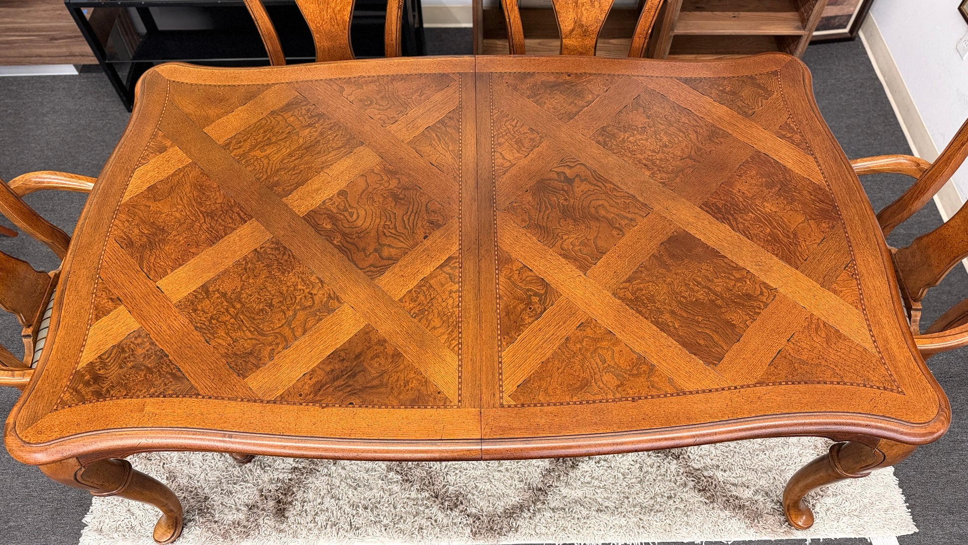 A 7-piece formal dining set featuring a marquetry wood inlay rectangular table with cabriole legs and six carved chairs with striped seats.