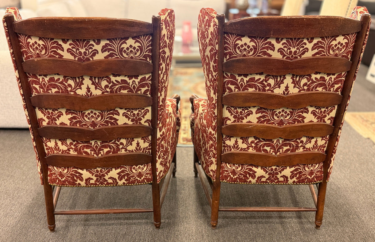 Pair of classic wingback armchairs upholstered in a bold burgundy and cream damask floral pattern detailed with nailhead trim and carved wooden legs in good condition.