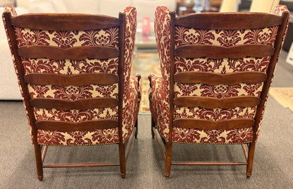 Pair of classic wingback armchairs upholstered in a bold burgundy and cream damask floral pattern detailed with nailhead trim and carved wooden legs in good condition.