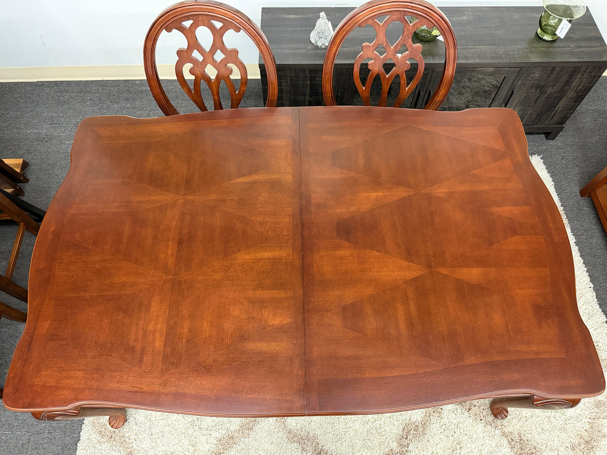 A traditional dark wood dining set including a rectangular table and four chairs with ornate backrests and light upholstered seats in excellent condition.