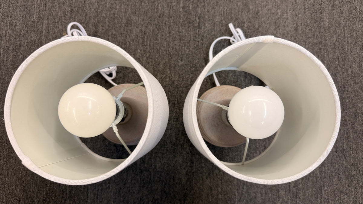A pair of matching table lamps featuring rounded textured ceramic bases and simple white drum shades in excellent condition.