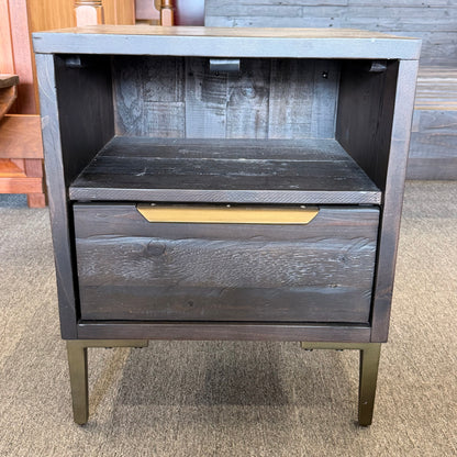 Wooden nightstand with a single drawer on a carpeted floor.