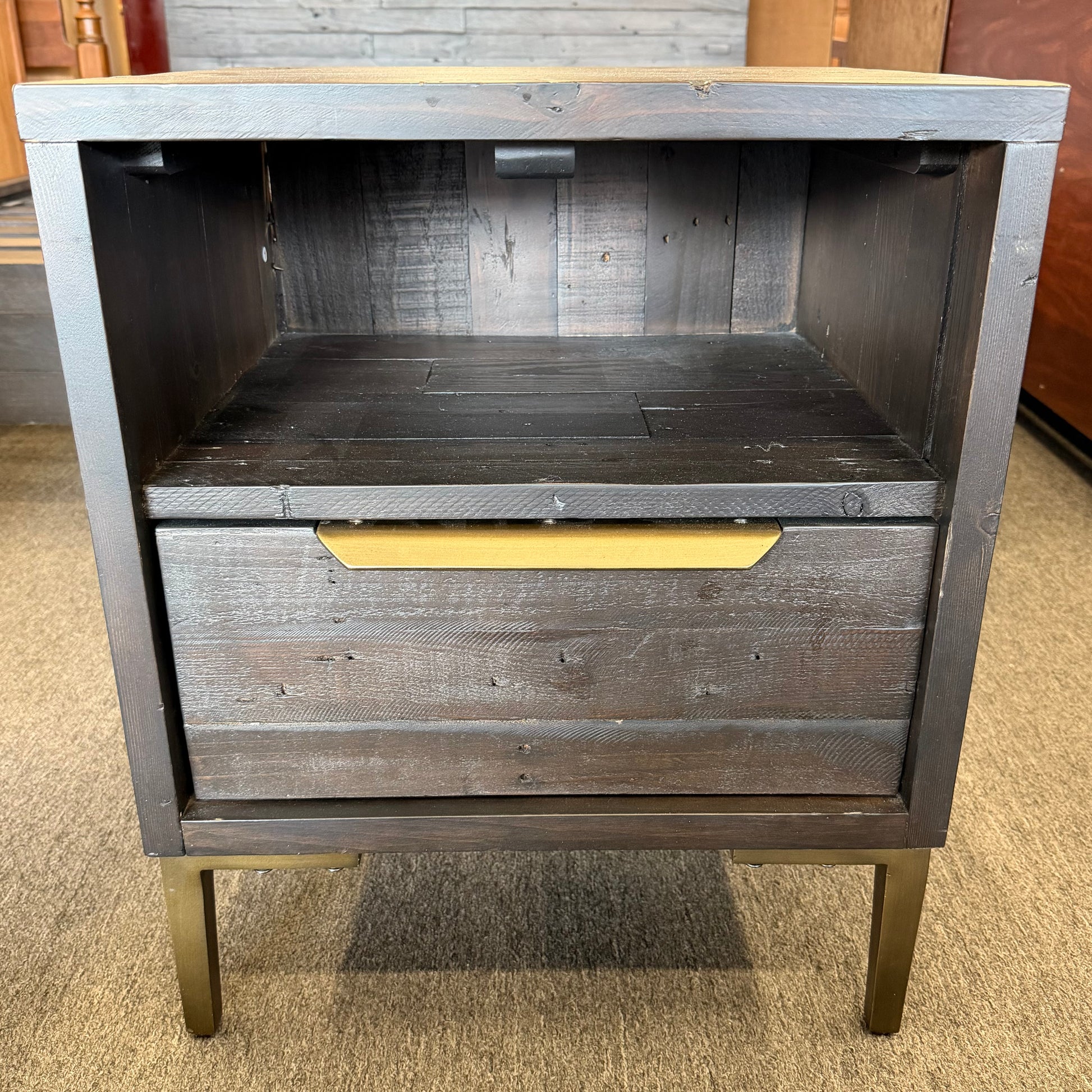 Wooden nightstand with a single drawer and gold handle on a carpeted floor.