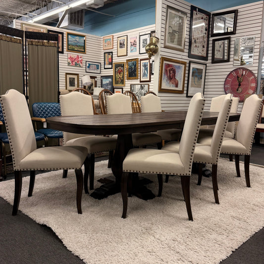 Dining room set with a round wooden table and beige chairs in a showroom setting.