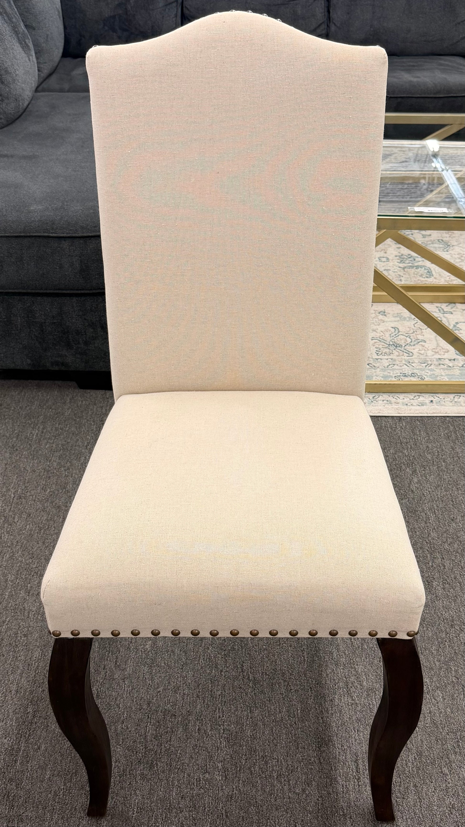 Beige upholstered chair with dark wood legs on a gray carpeted floor.