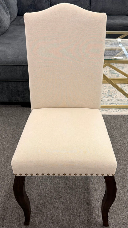 Beige upholstered chair with dark wood legs on a gray carpeted floor.