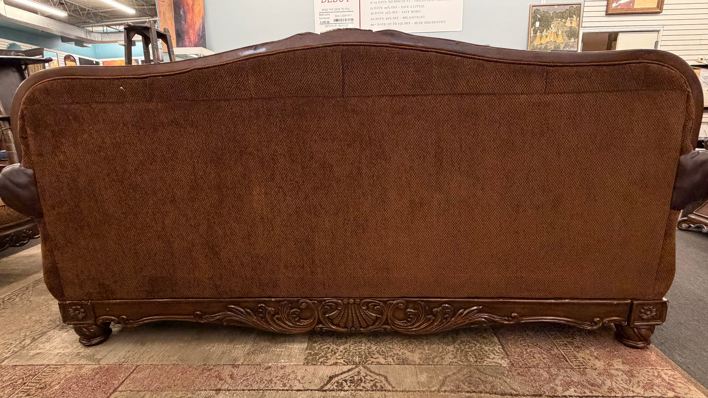 Brown upholstered sofa with decorative carvings in a room setting.