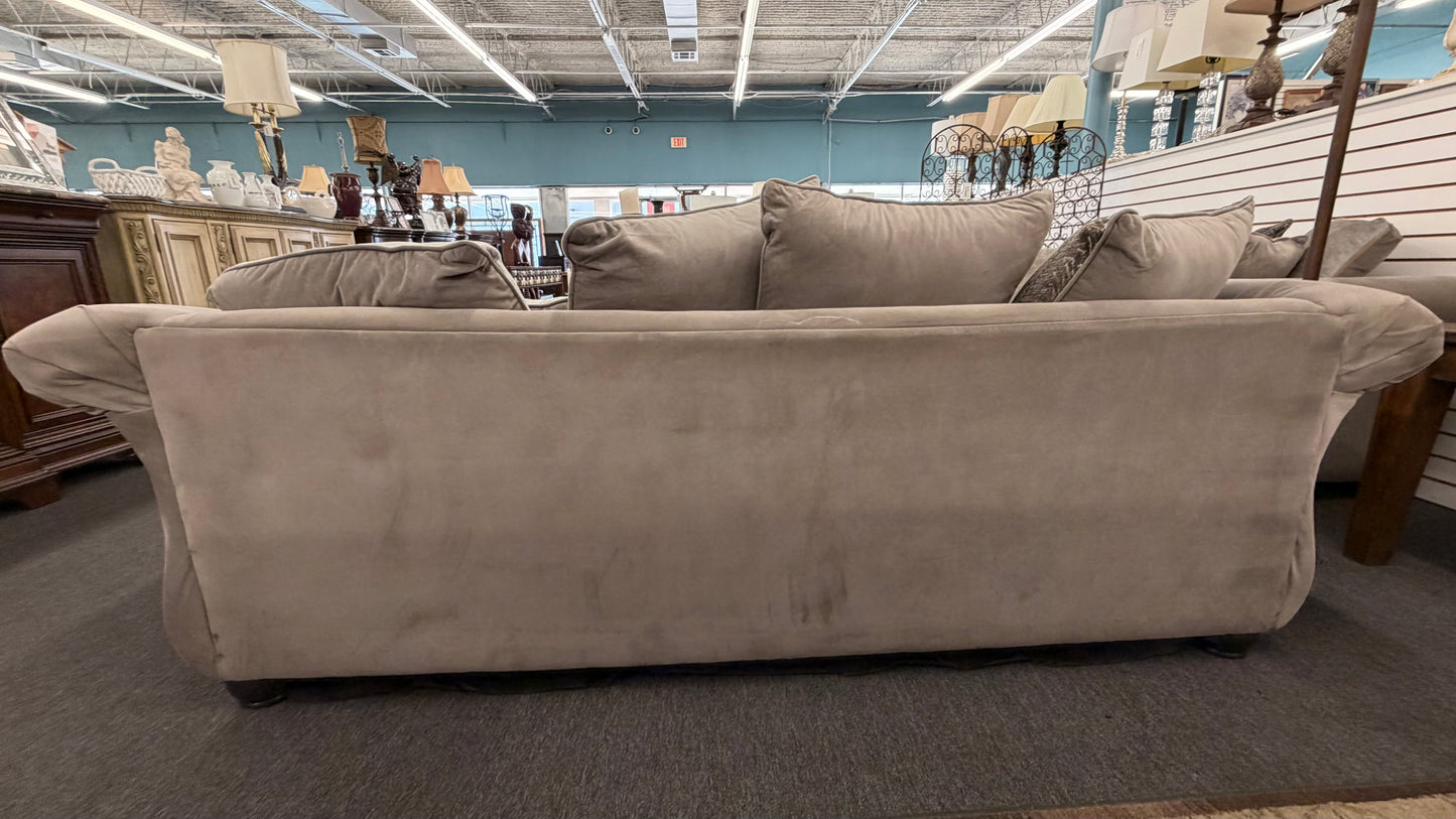 Beige sofa in a furniture store setting with various items in the background.