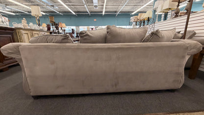 Beige sofa in a furniture store setting with various items in the background.