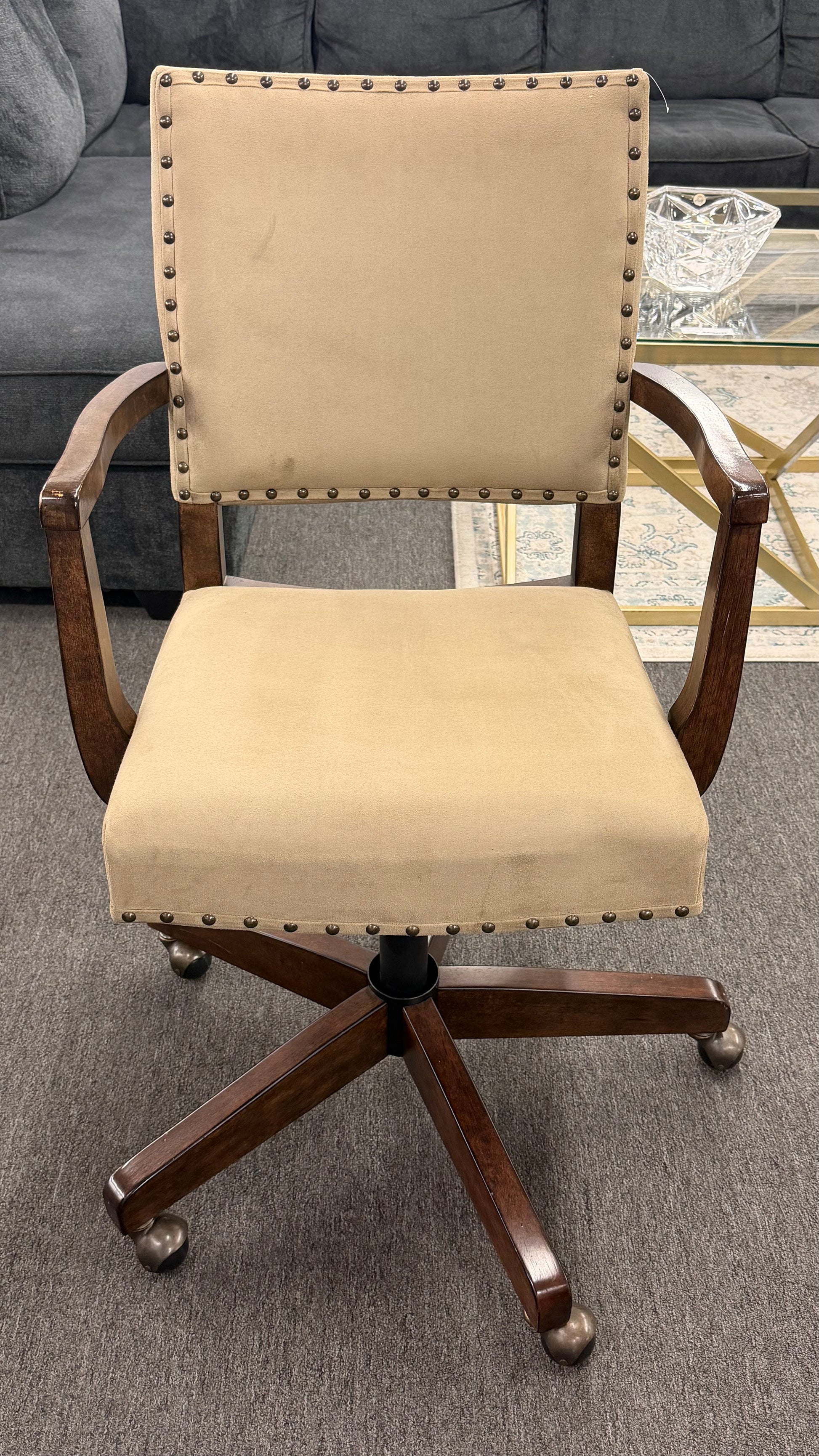 Beige office chair with wooden frame and wheels on a gray floor.
