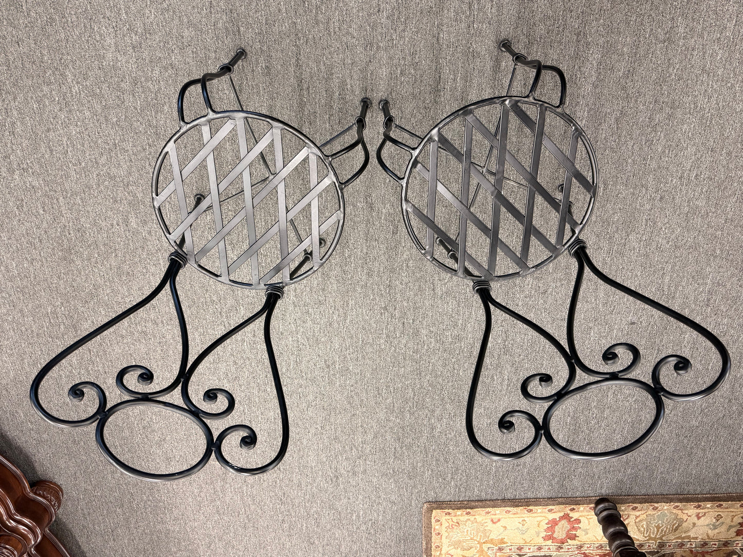 Decorative metal wall hooks with intricate designs on a textured wall.