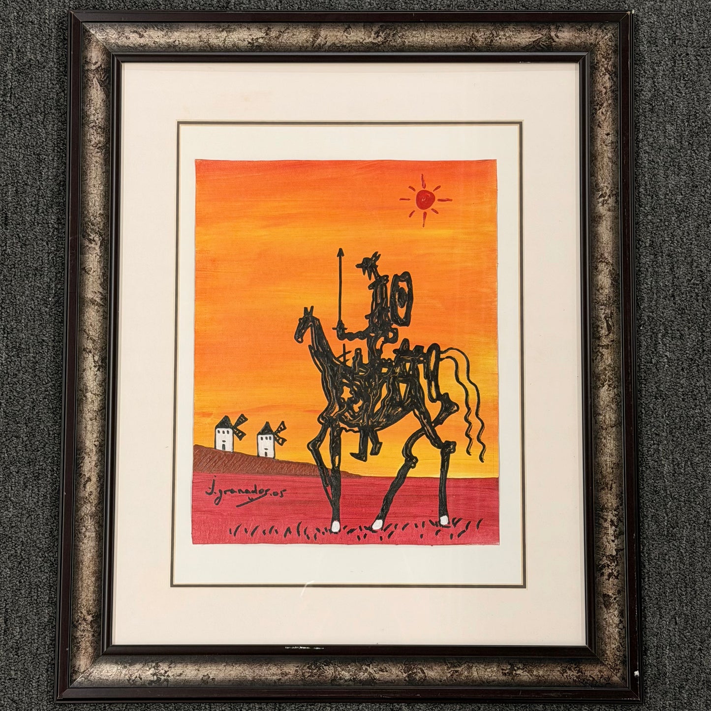 Framed artwork of Don Quixote on horseback against an orange sunset with windmills.