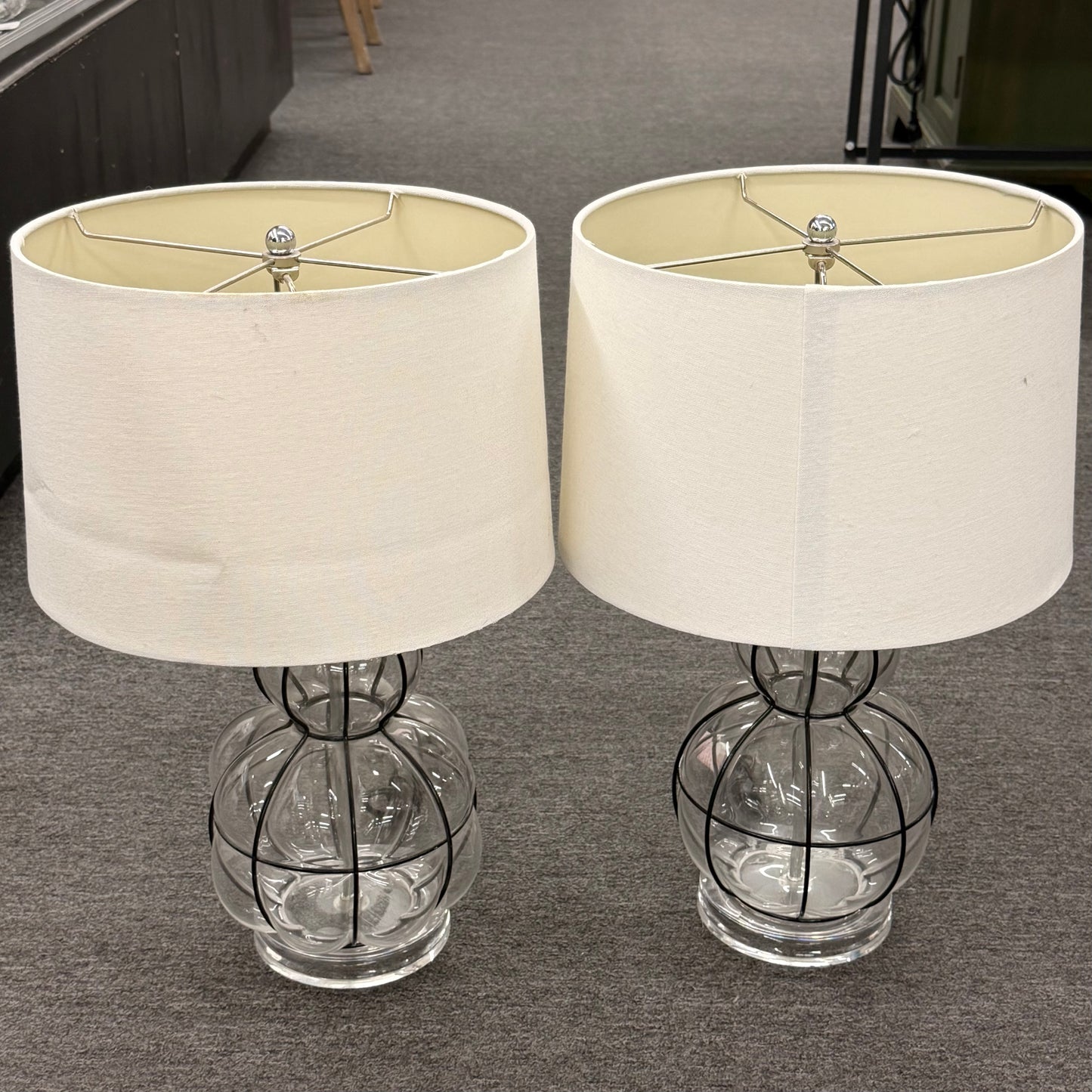 Two table lamps with glass bases and white lampshades on a gray floor.